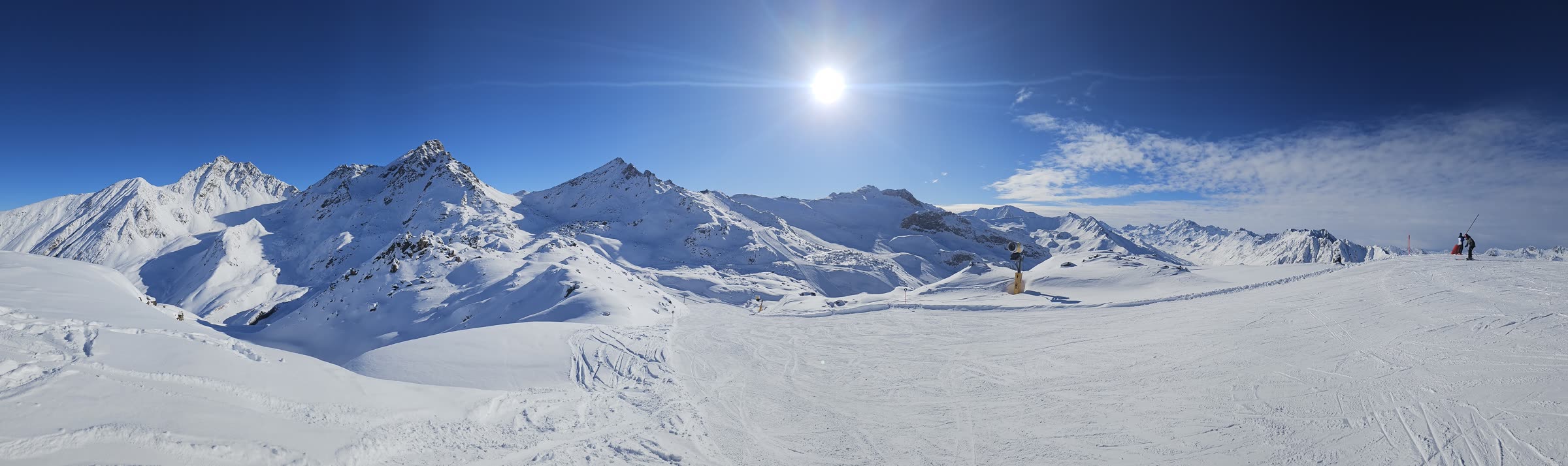 Wide panorama of sunlit alpine peaks and pistes