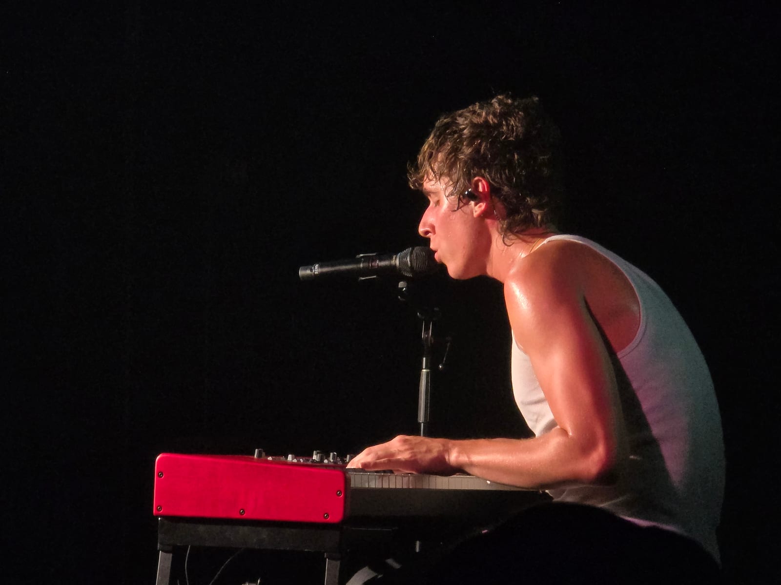 A singer at a red keyboard, side lit against a black stage