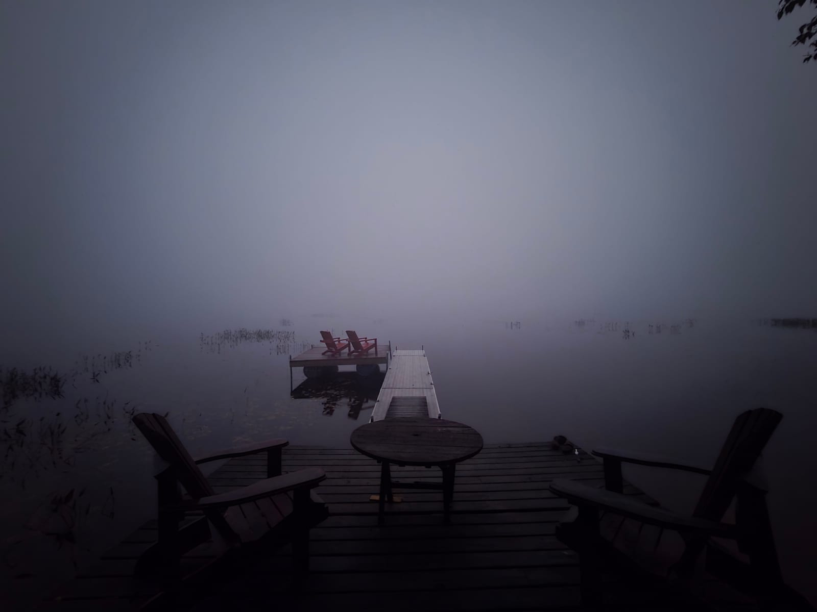 A dock running out into dense morning fog on a lake, two red chairs on the swim raft