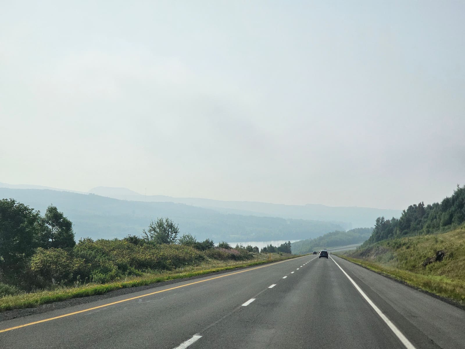 An empty highway running into hazy blue hills, a river in the valley below