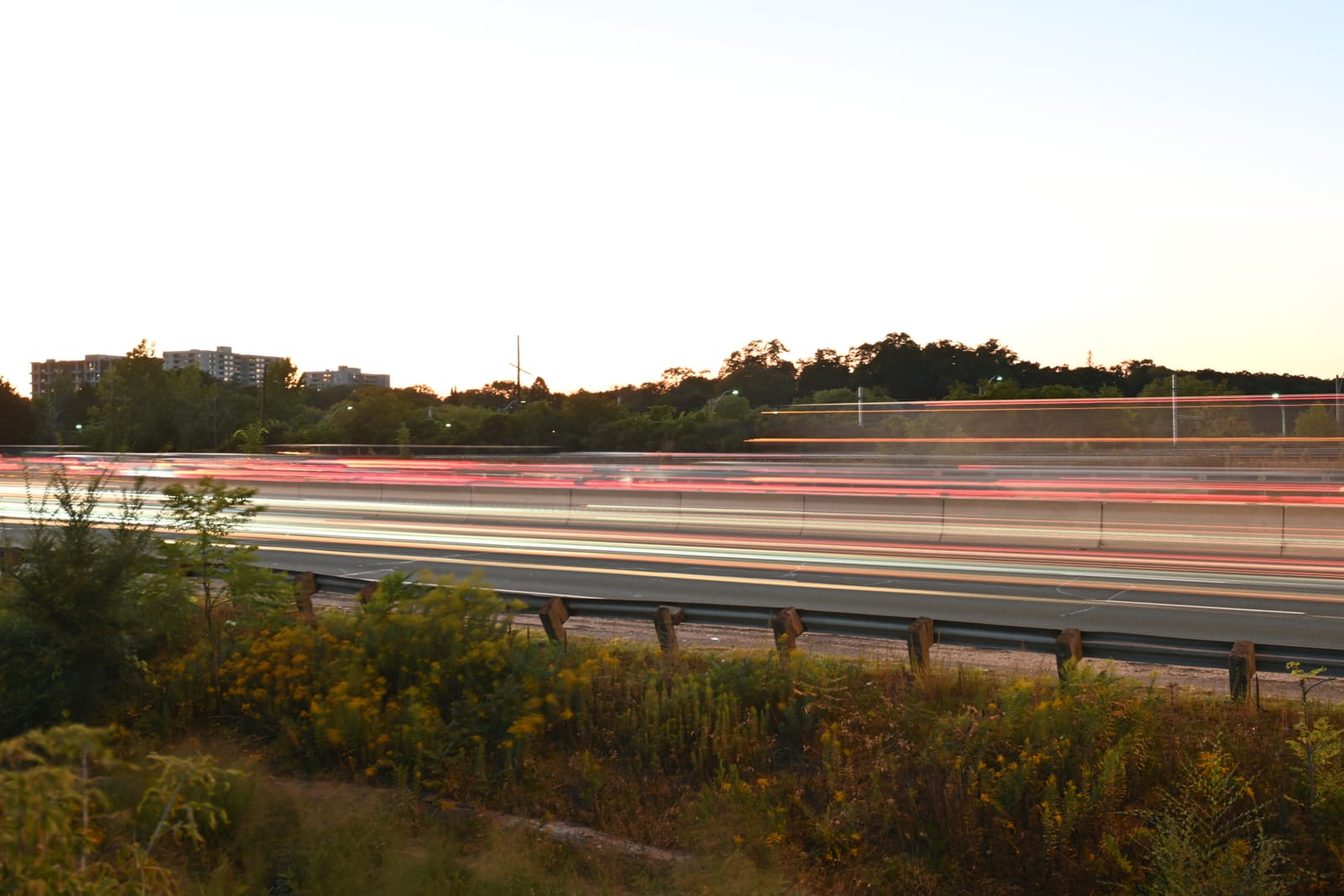 Long exposure of highway traffic at dusk, red and white light trails running past a guardrail