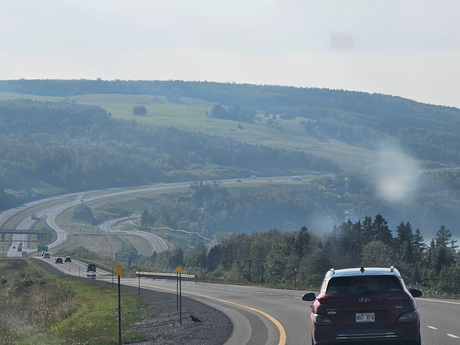 The highway ahead from the driver's seat, an SUV in front and green hills either side